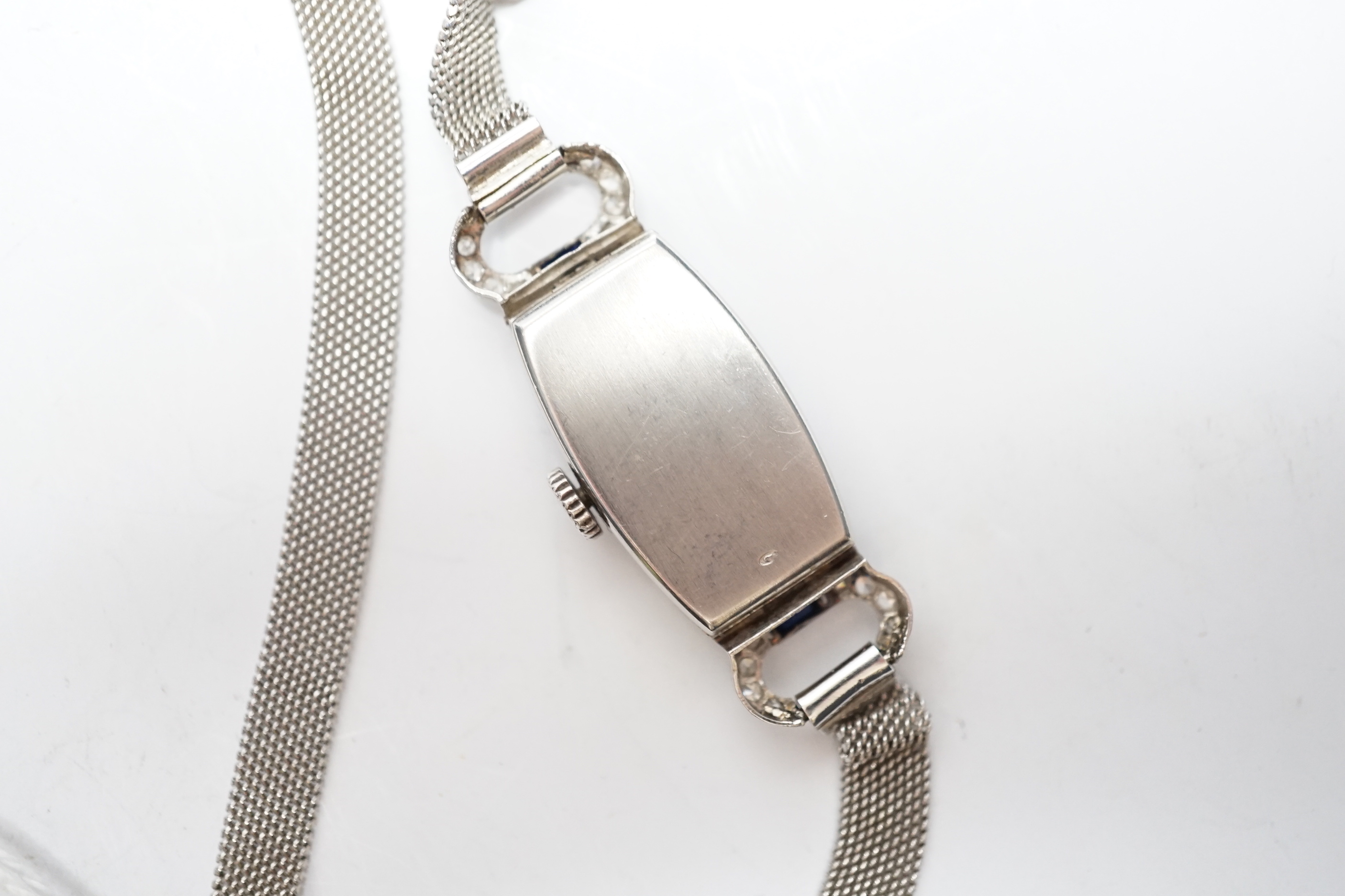 A lady's mid 20th century white metal (Swiss platinum mark), sapphire and diamond cluster set manual wind cocktail watch, with Arabic dial, on and adjustable 9ct mesh link bracelet, gross weight 18 grams.